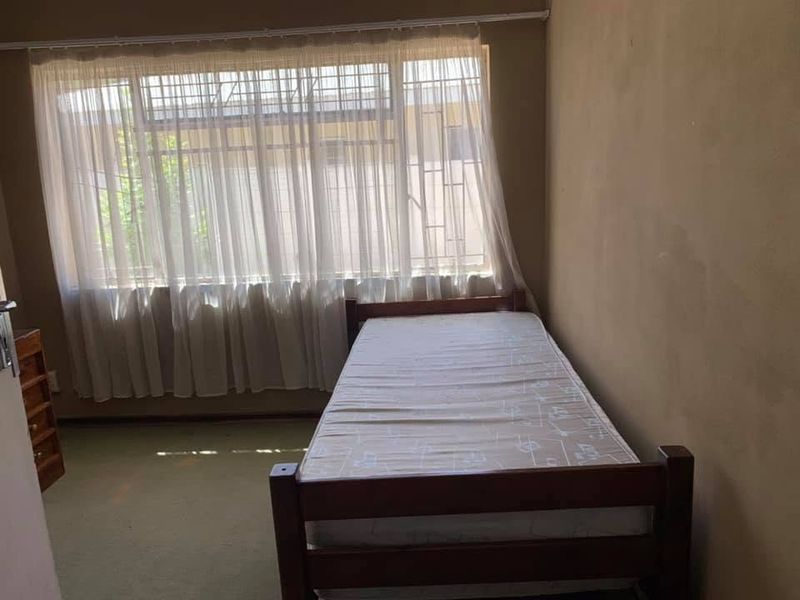 A simple bedroom featuring a large window with security bars and carpeted flooring, offering a functional space ready for cosmetic updates.