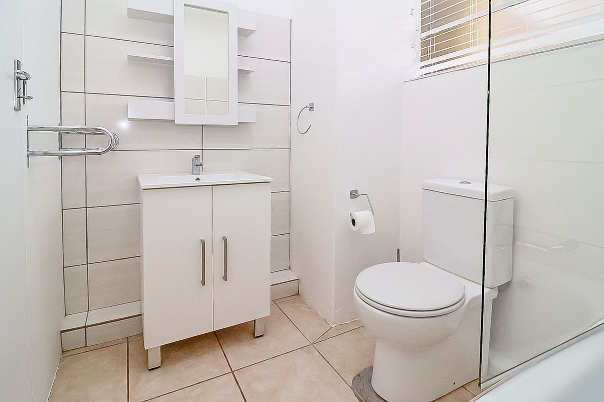 A clean, modern bathroom featuring a white vanity cabinet, wall-mounted mirror, tiled walls, and a glass-enclosed shower area.