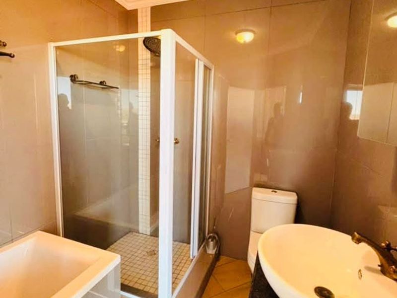 A functional bathroom featuring a shower enclosure, bathtub, toilet, and a vessel sink set on a granite vanity countertop with tiled finishes.