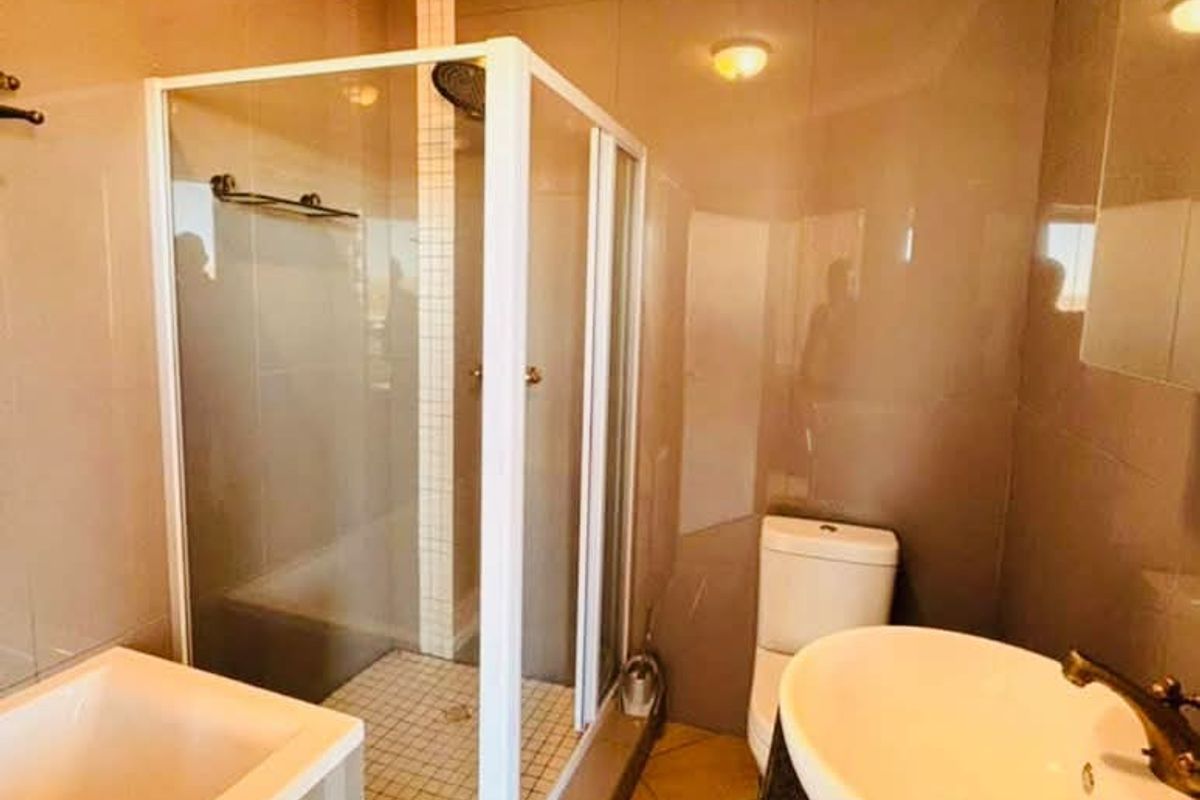 A functional bathroom featuring a shower enclosure, bathtub, toilet, and a vessel sink set on a granite vanity countertop with tiled finishes.