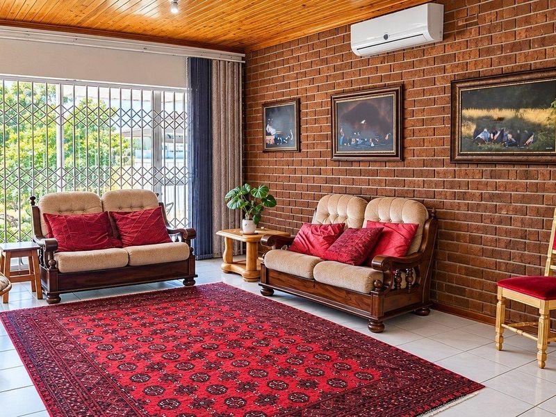 A living room featuring an exposed brick feature wall, timber ceiling, tiled floors, and a split-system air conditioner, with access to the garden via security gates.