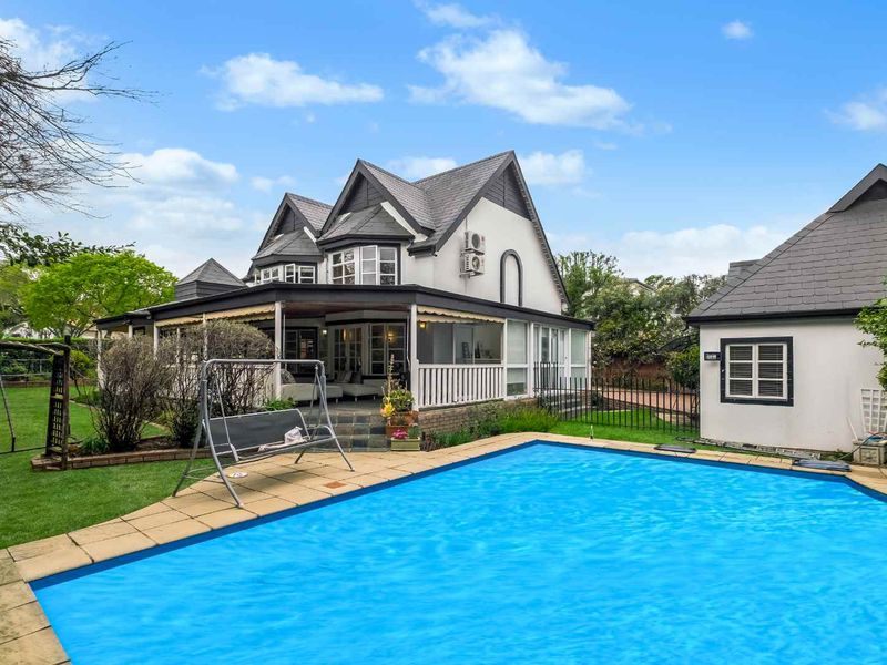A well-maintained rear garden featuring a swimming pool, paved surround, and a covered patio area attached to the main residence.