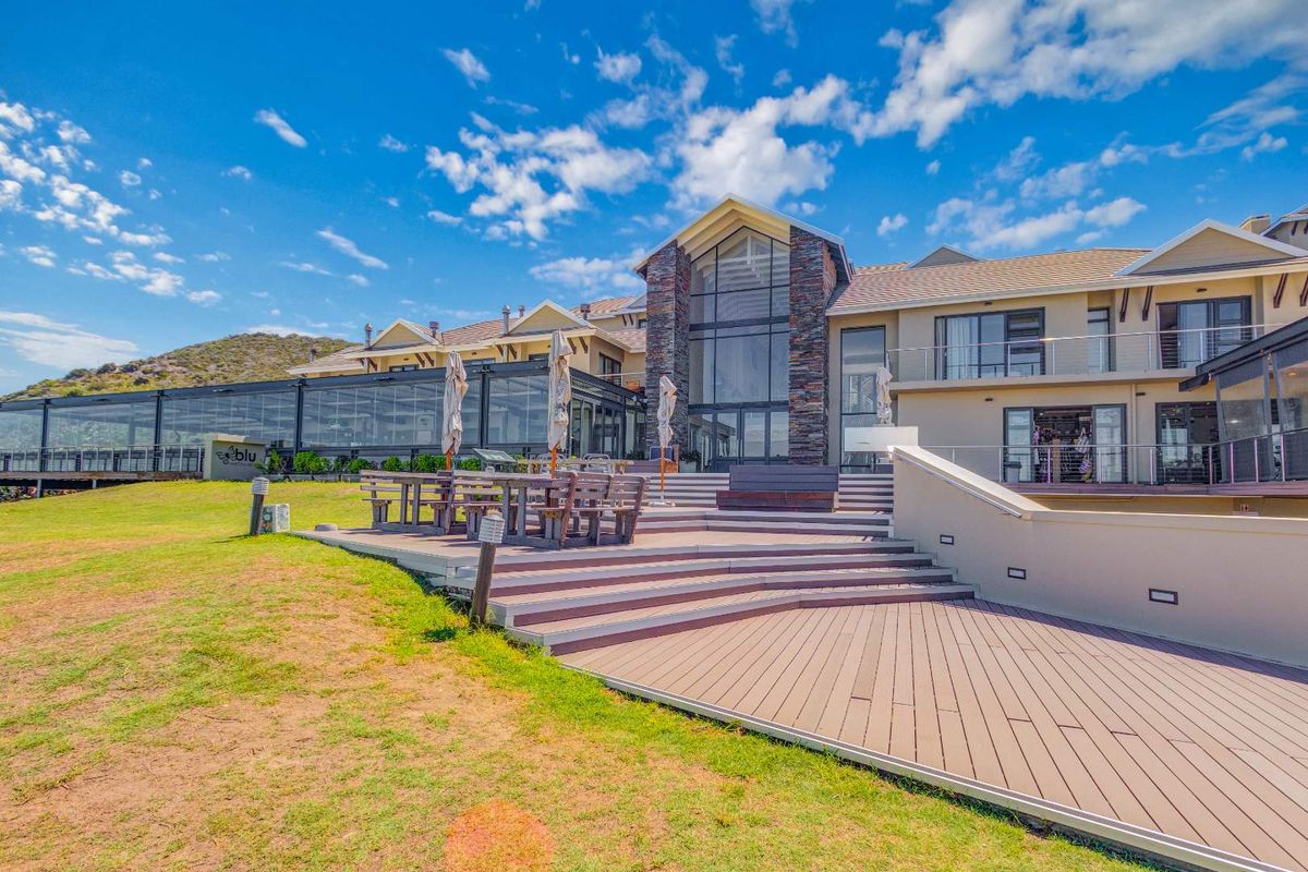 A spacious rear exterior view of the townhouse featuring a large composite deck, stone-clad facade, and expansive glass windows overlooking the landscaped grounds.