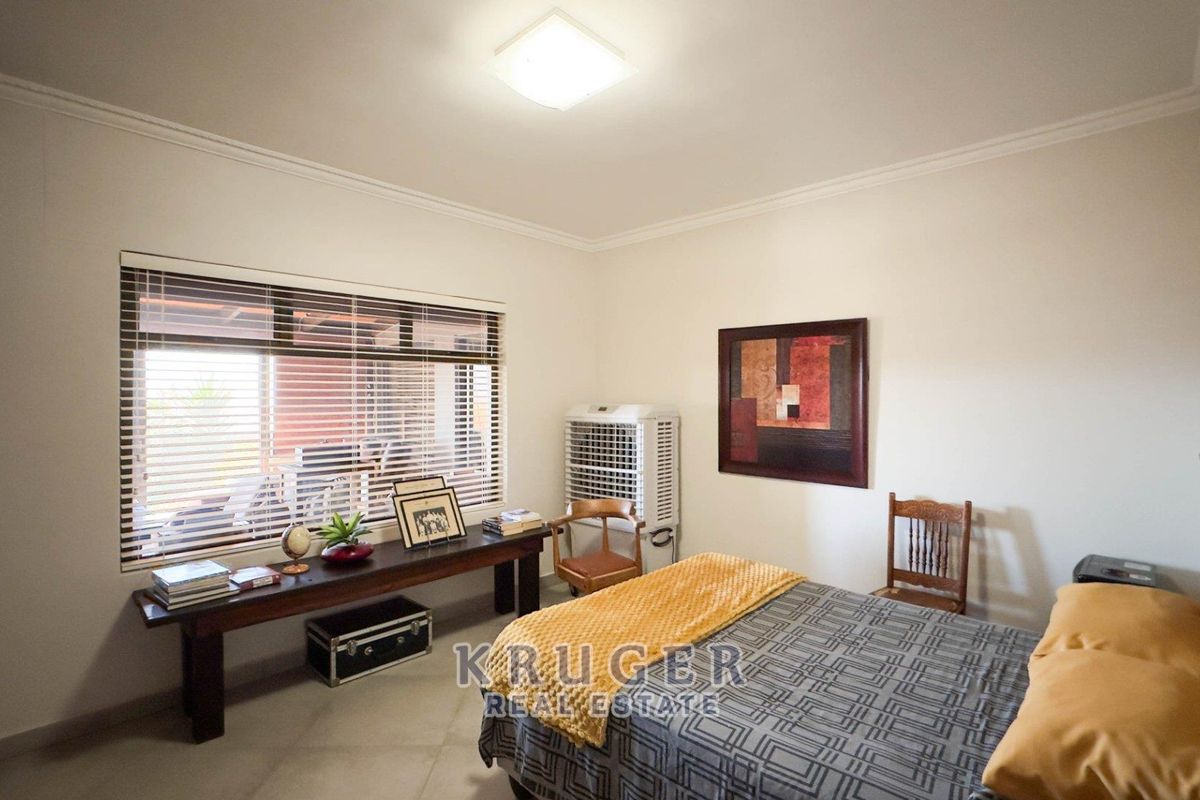 A well-lit bedroom featuring tiled flooring, a large window with fitted blinds, and a ceiling-mounted light fixture.