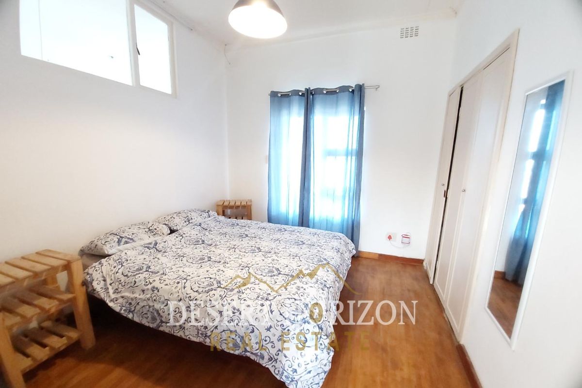 A bedroom featuring built-in cupboards, wooden flooring, and a high-level window, providing a functional and well-lit living space.