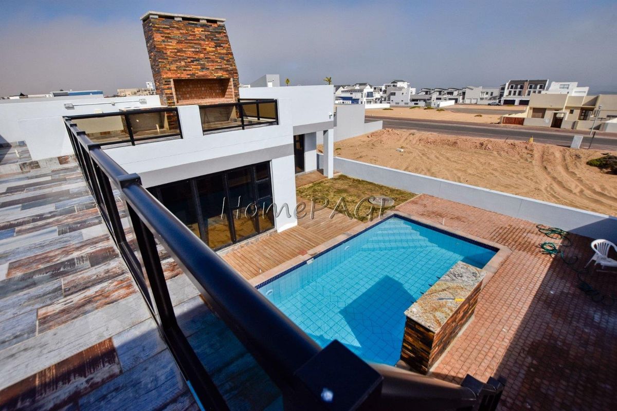 Aerial view of a modern property featuring a swimming pool, outdoor fireplace, wooden decking, and a paved patio area.