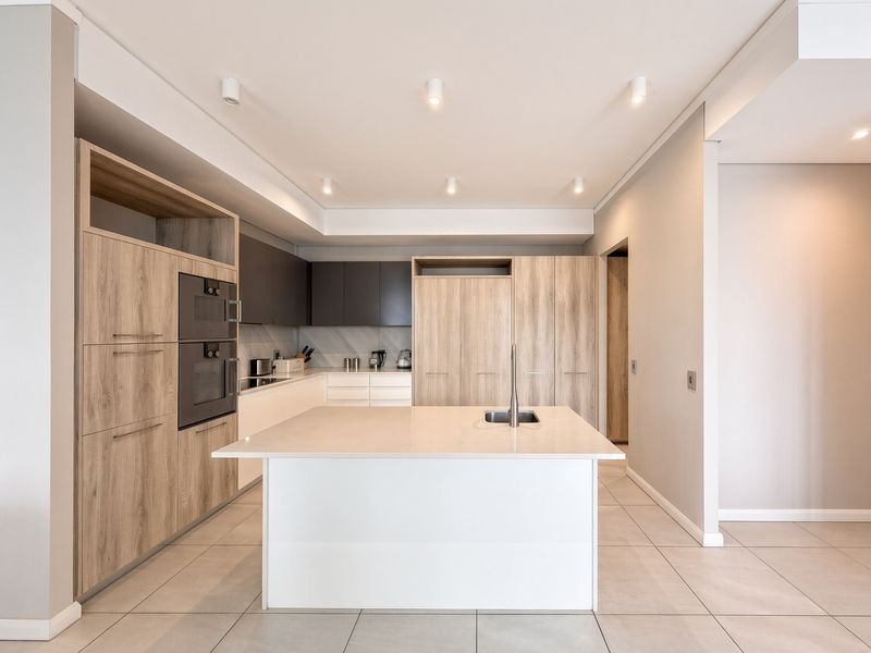 Modern kitchen featuring a central island with an undermount sink, built-in appliances, sleek laminate cabinetry, and recessed lighting throughout.
