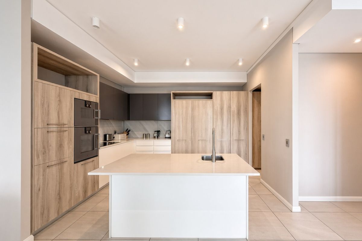 Modern kitchen featuring a central island with an undermount sink, built-in appliances, sleek laminate cabinetry, and recessed lighting throughout.