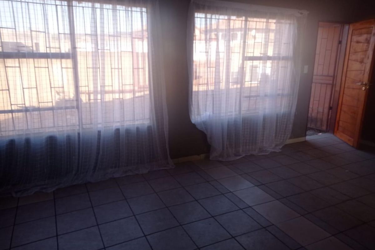 A living area featuring tiled flooring, large windows with security bars, and a wooden door leading to an exterior space.