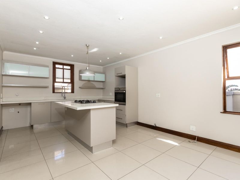 Modern open-plan kitchen featuring neutral cabinetry, a central island with a gas hob, built-in oven, and sleek tiled flooring throughout.