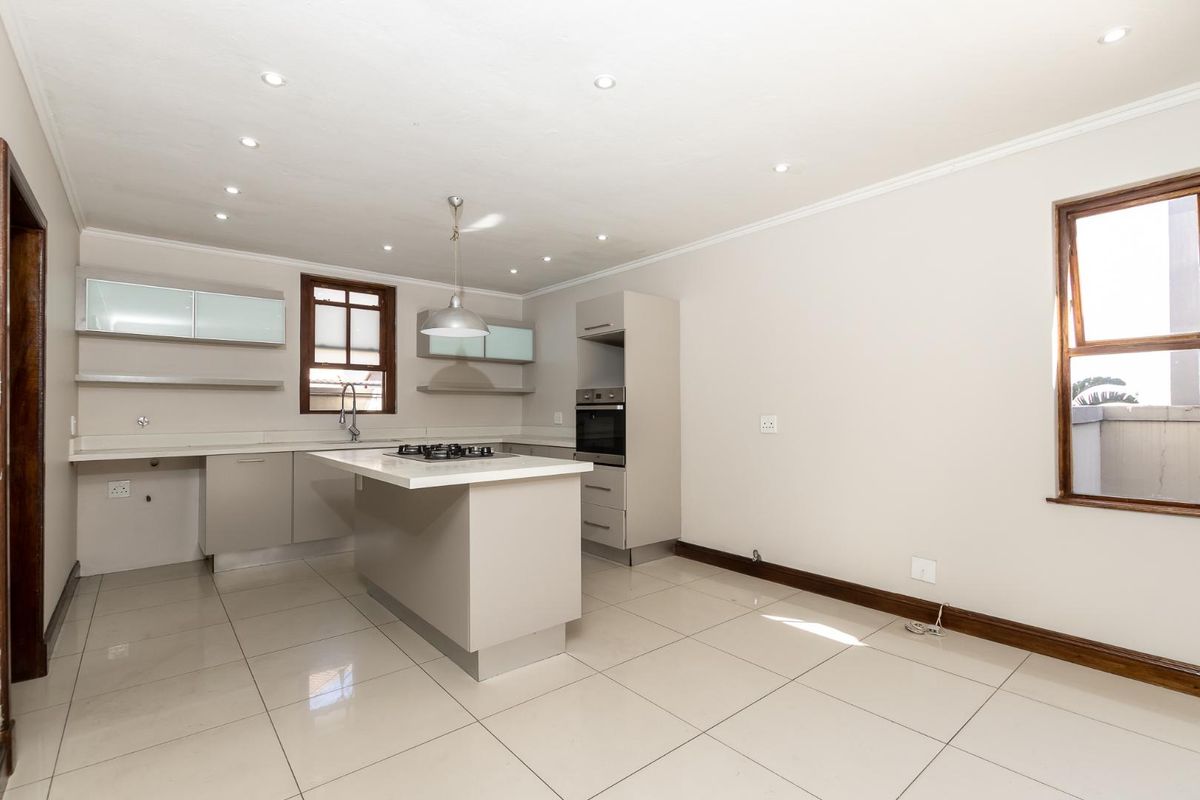Modern open-plan kitchen featuring neutral cabinetry, a central island with a gas hob, built-in oven, and sleek tiled flooring throughout.