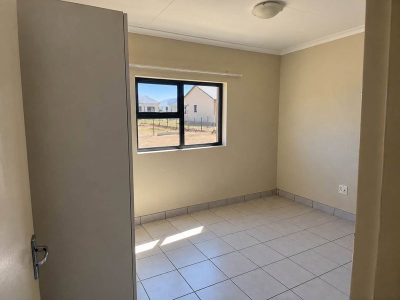 A clean, empty bedroom featuring neutral tiled flooring, a built-in cupboard, and an aluminium-framed window providing natural light.