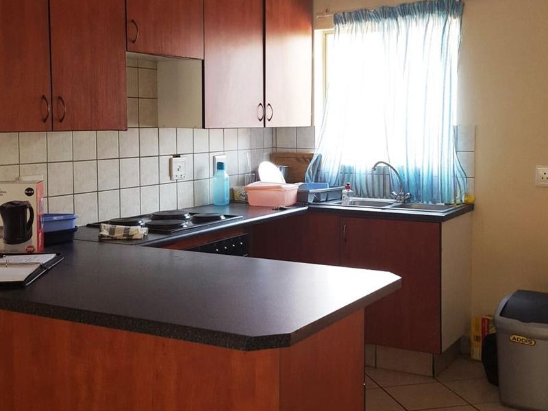 A functional kitchen featuring wood-look laminate cabinetry, dark countertops, a ceramic tile backsplash, and tiled flooring with a built-in electric hob.
