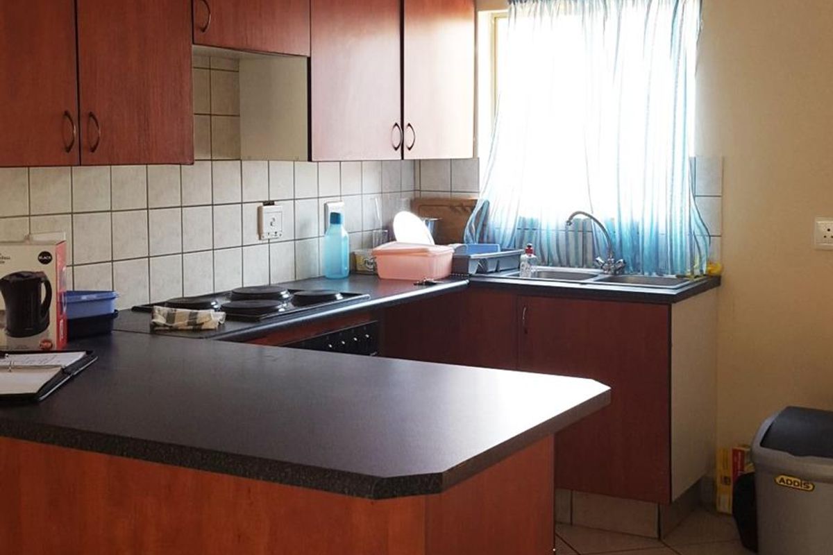 A functional kitchen featuring wood-look laminate cabinetry, dark countertops, a ceramic tile backsplash, and tiled flooring with a built-in electric hob.
