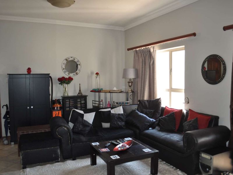 A comfortable living room featuring tiled flooring, decorative cornice, and a window with a curtain rod, providing a functional and well-lit space.
