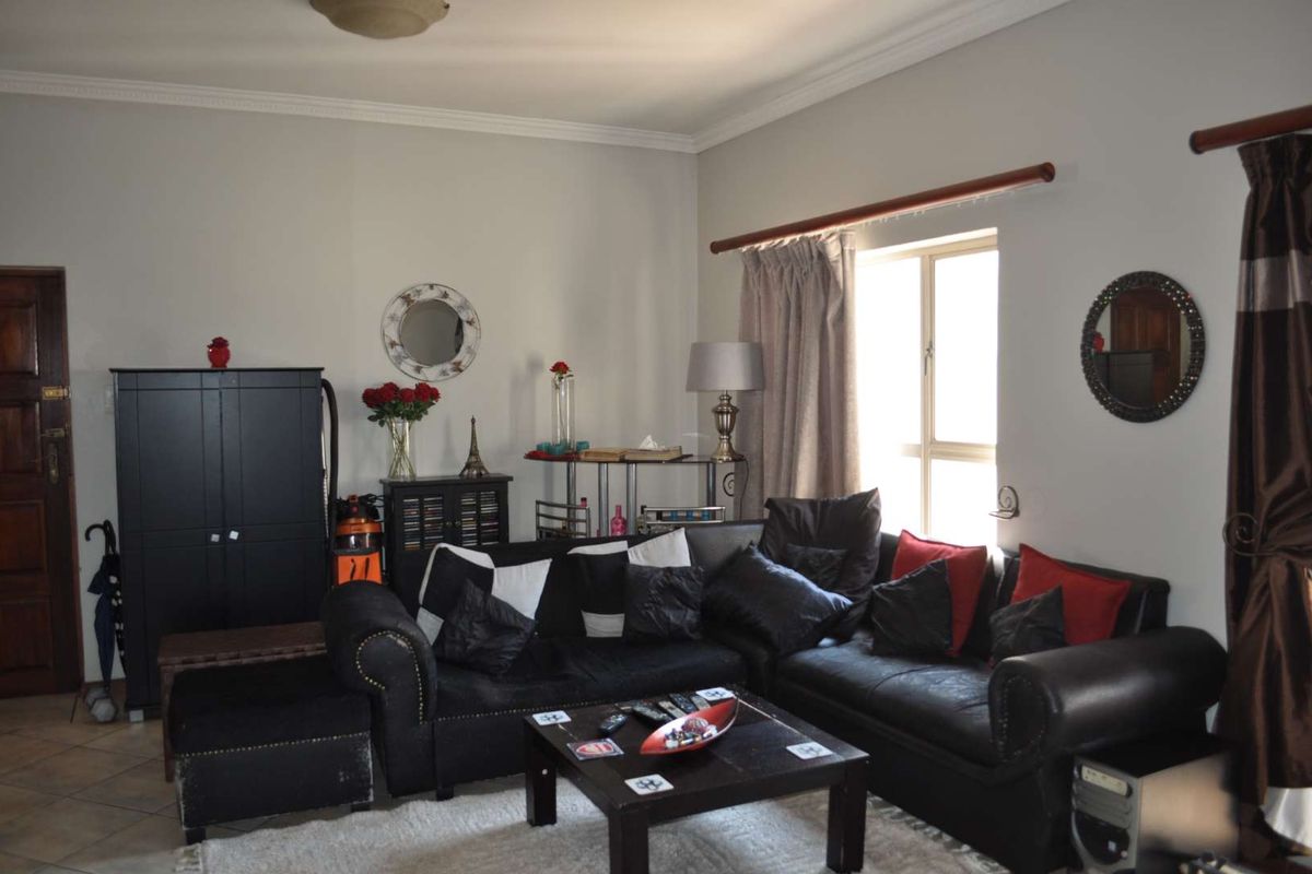 A comfortable living room featuring tiled flooring, decorative cornice, and a window with a curtain rod, providing a functional and well-lit space.