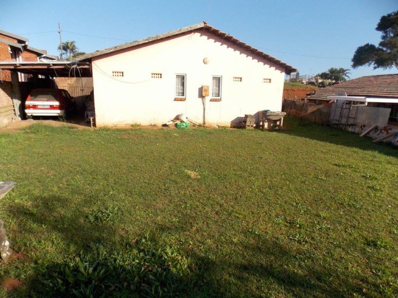 Rear view of the property featuring a lawn, a carport structure, and a concrete wash basin attached to the exterior wall.
