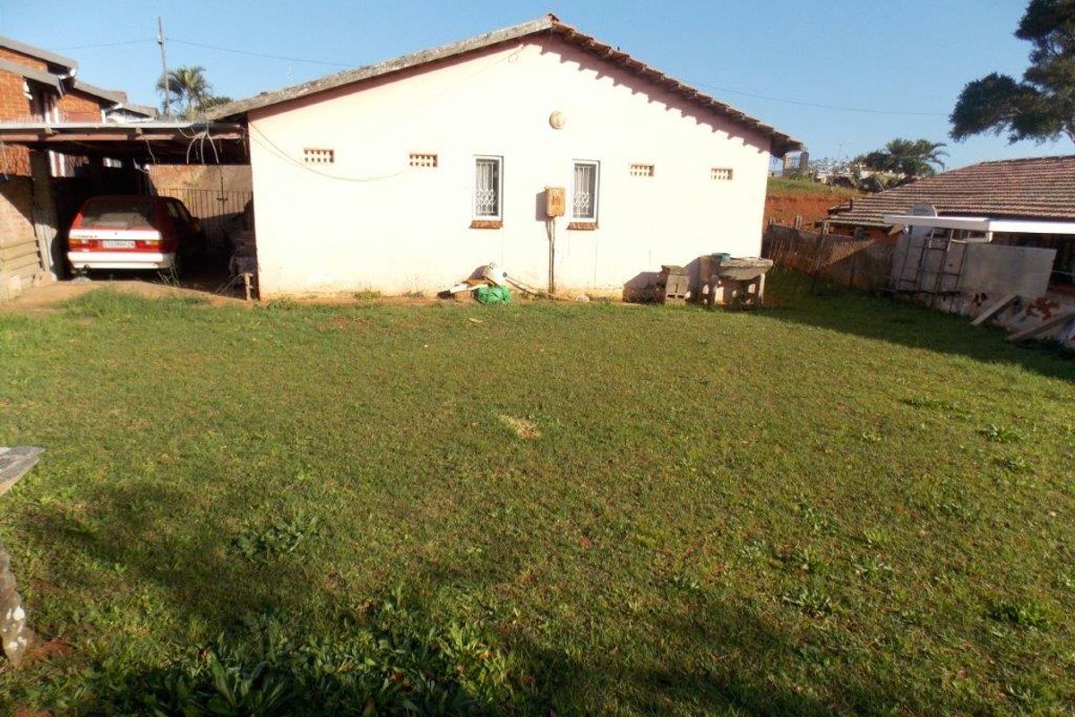 Rear view of the property featuring a lawn, a carport structure, and a concrete wash basin attached to the exterior wall.