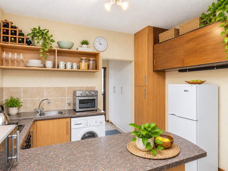 A functional kitchen featuring wood-tone cabinetry, laminate countertops, a tiled backsplash, and integrated storage solutions, offering a practical layout for daily use.