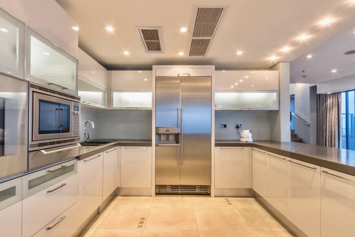 Modern kitchen featuring high-gloss cabinetry, integrated stainless steel refrigerator, built-in microwave, stone countertops, and recessed ceiling lighting.