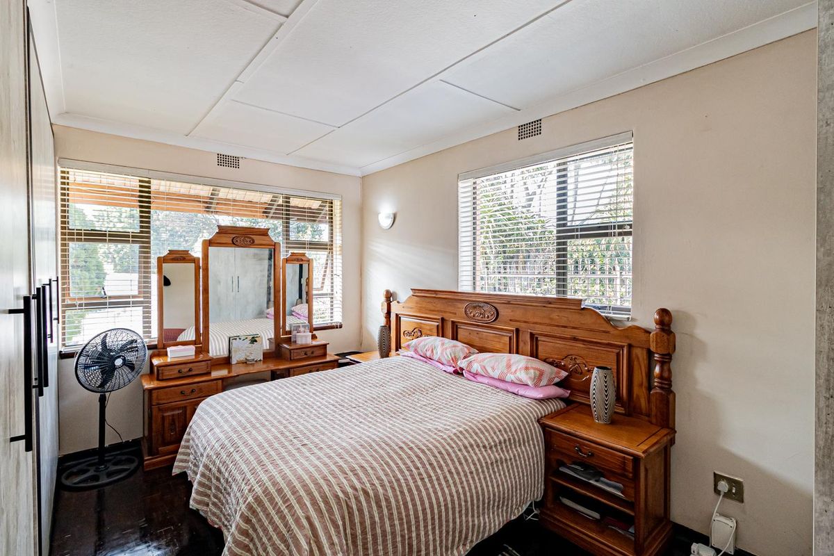 A bedroom featuring large windows with blinds, built-in wardrobe, and dark flooring.