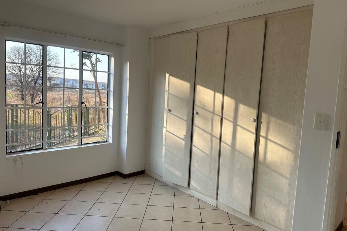 An empty bedroom featuring built-in cupboards, tiled flooring, and a window with security bars, offering a blank canvas for personalization.