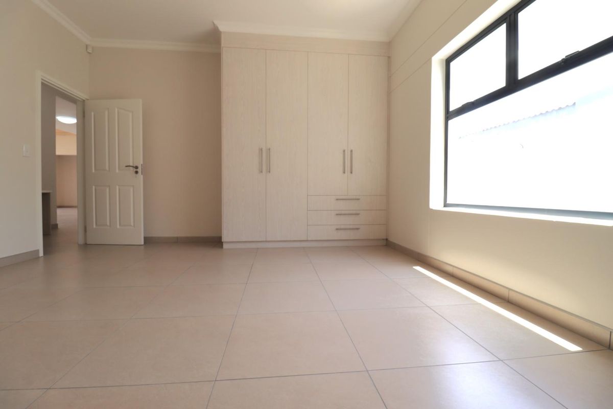 A bright, empty bedroom featuring neutral floor tiles, built-in cabinetry, and a large window allowing for ample natural light.