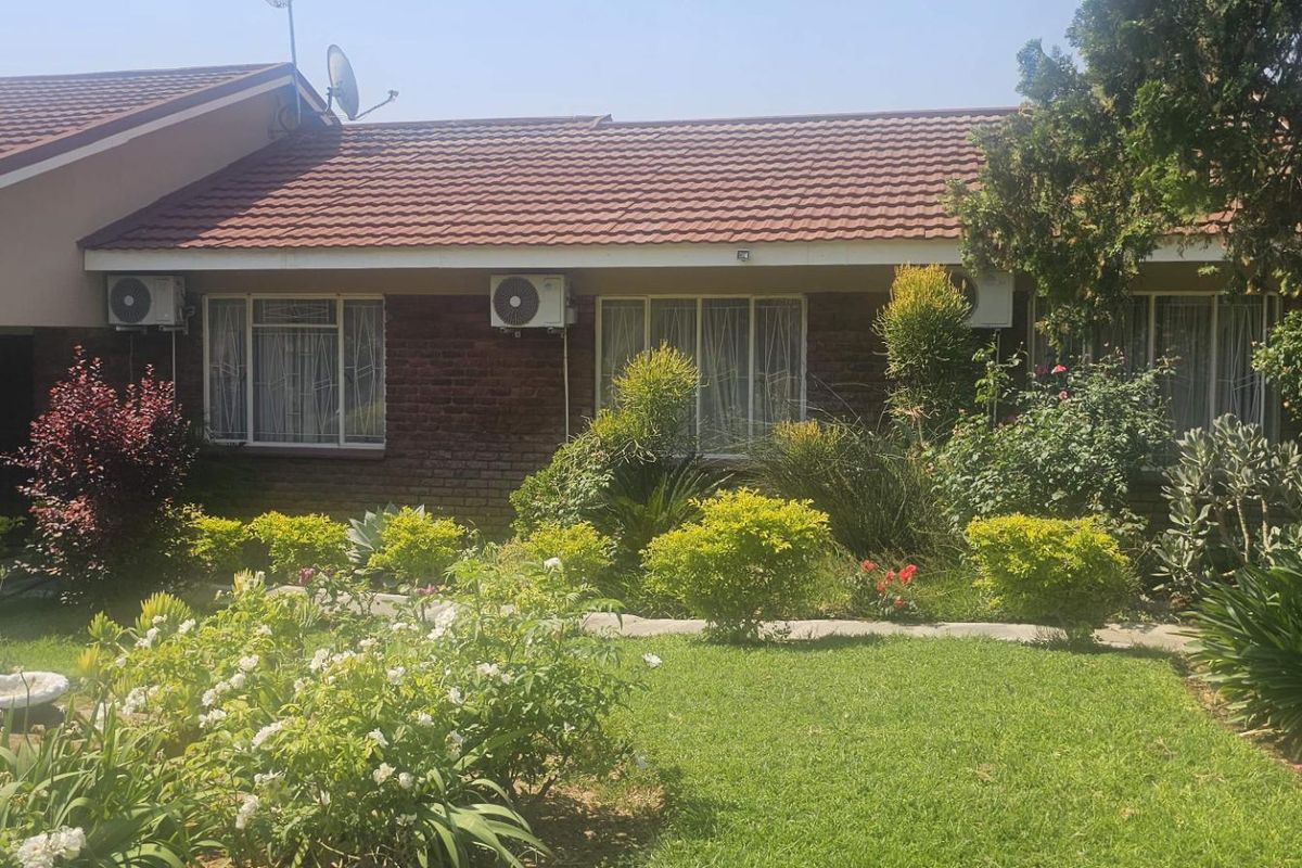 A view of the rear facade of the house featuring a brick exterior, tiled roof, and a well-maintained garden area.