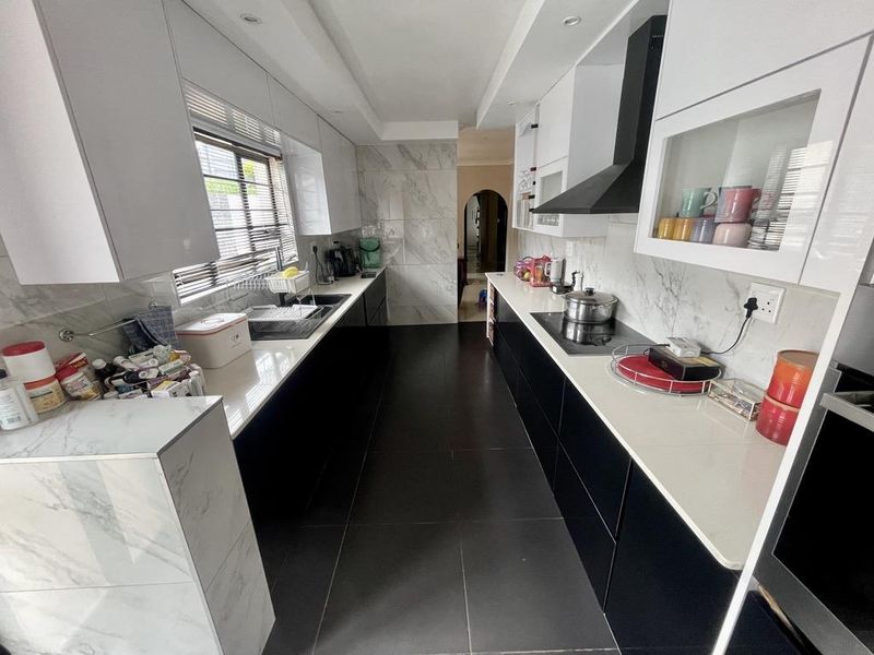 Modern galley-style kitchen featuring high-contrast black and white cabinetry, marble-look splashbacks, stone countertops, and integrated appliances.