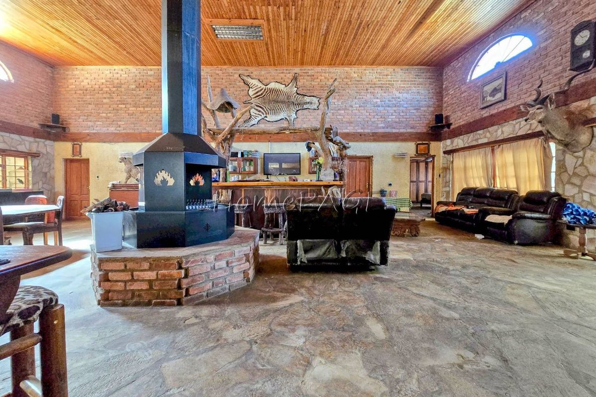 Spacious living area featuring a central freestanding fireplace, exposed brick walls, timber ceiling, and stone flooring, with an integrated bar counter.
