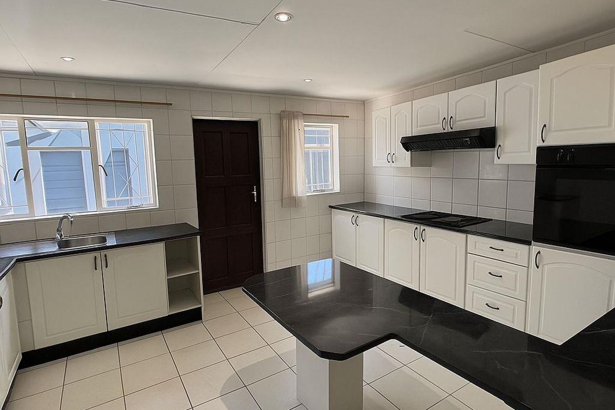 A clean, functional kitchen featuring white cabinetry, dark countertops, a built-in oven, extractor fan, and tiled flooring throughout.