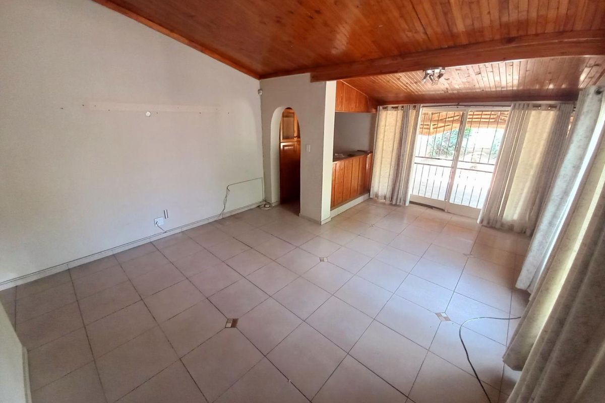 Spacious living area featuring a vaulted timber ceiling, tiled flooring, and an arched entryway leading to a built-in bar area.