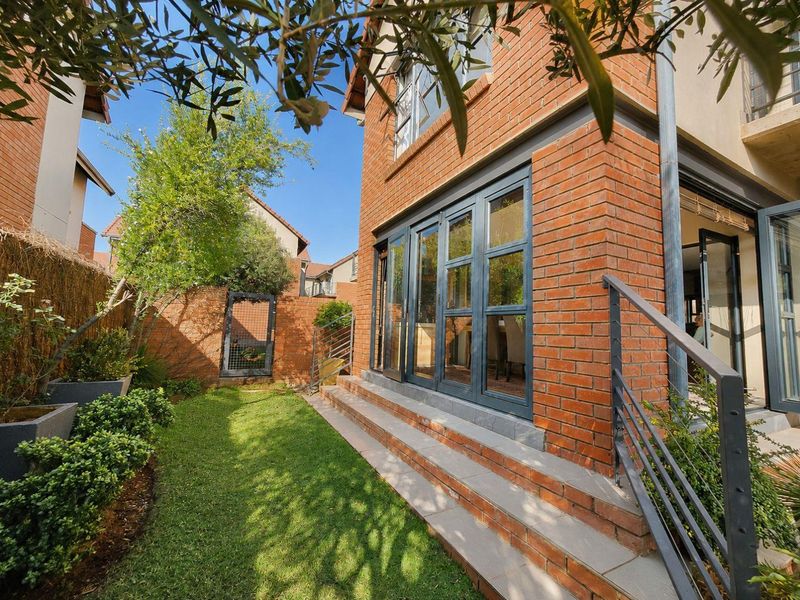 Rear view of the townhouse featuring a brick facade, folding glass doors leading to the interior, and a small landscaped garden with brick steps.