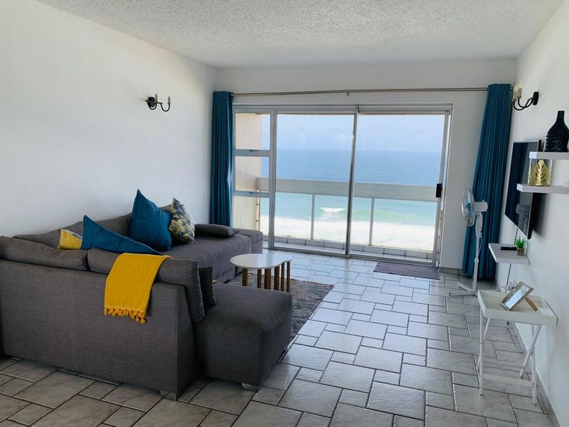 Bright living room featuring tiled flooring and large sliding glass doors that open onto a balcony with direct ocean views.