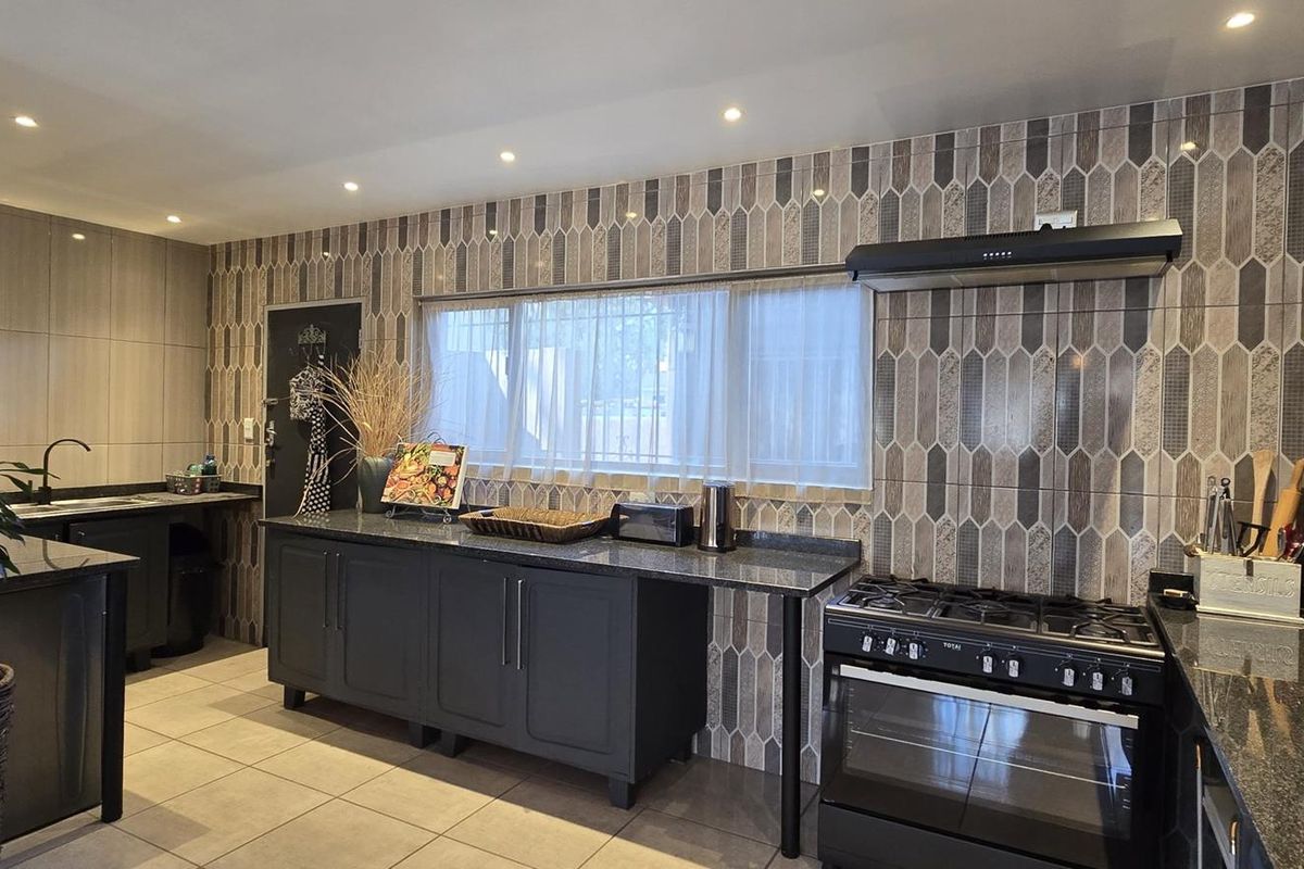 Modern kitchen featuring dark cabinetry, granite countertops, a gas stove with extractor fan, and decorative tiled backsplash with recessed lighting.