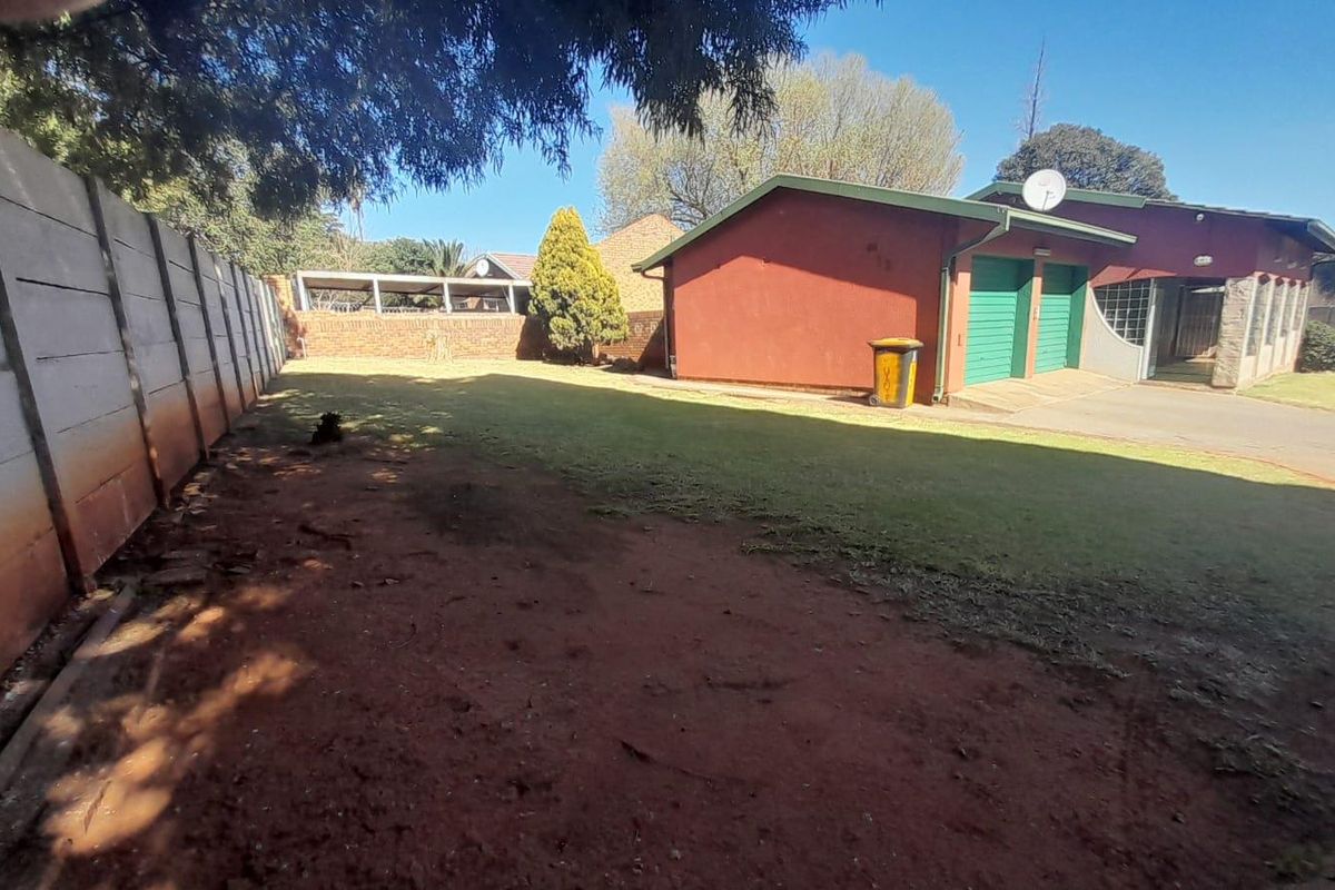 Rear exterior view of the property featuring a double garage, lawn area, and perimeter boundary walls.