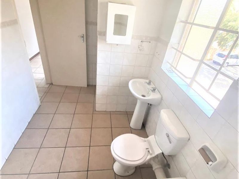 A functional bathroom featuring a pedestal basin, toilet, and bathtub, with tiled finishes and a window with security bars. Requires cosmetic updates.