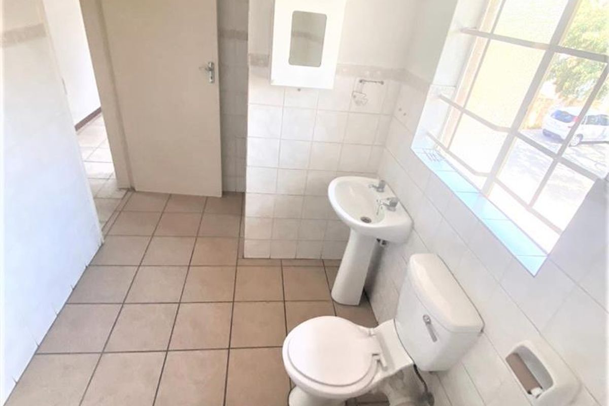A functional bathroom featuring a pedestal basin, toilet, and bathtub, with tiled finishes and a window with security bars. Requires cosmetic updates.