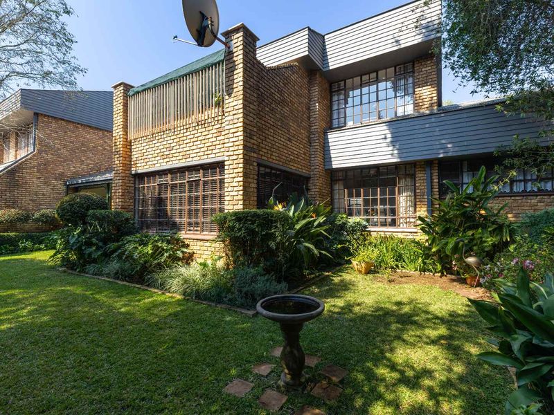 Rear view of the townhouse featuring a brick facade, metal-framed windows, an upper-level balcony, and a well-maintained private garden.