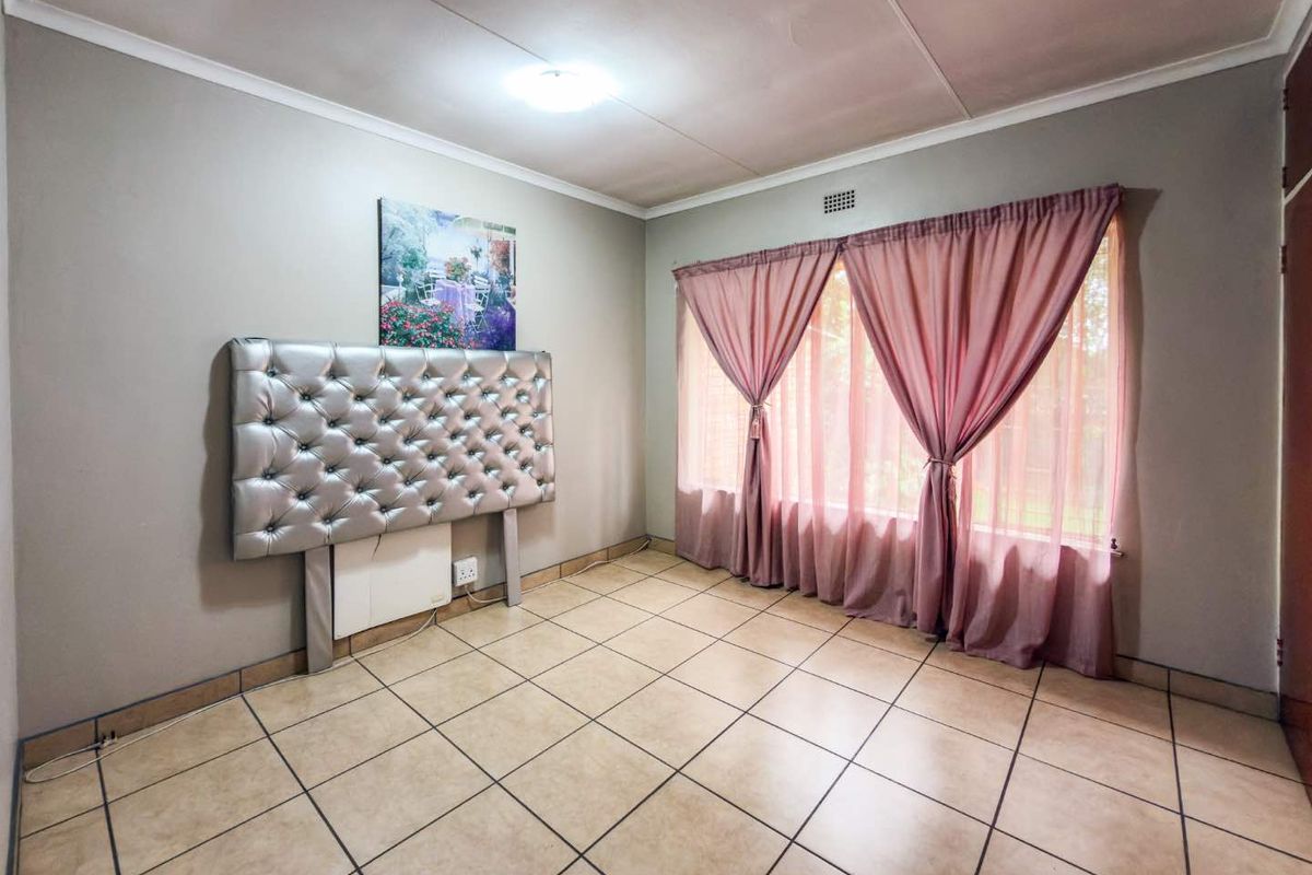 A bedroom featuring tiled flooring, neutral wall tones, and a large window with curtains, providing a functional and well-lit living space.