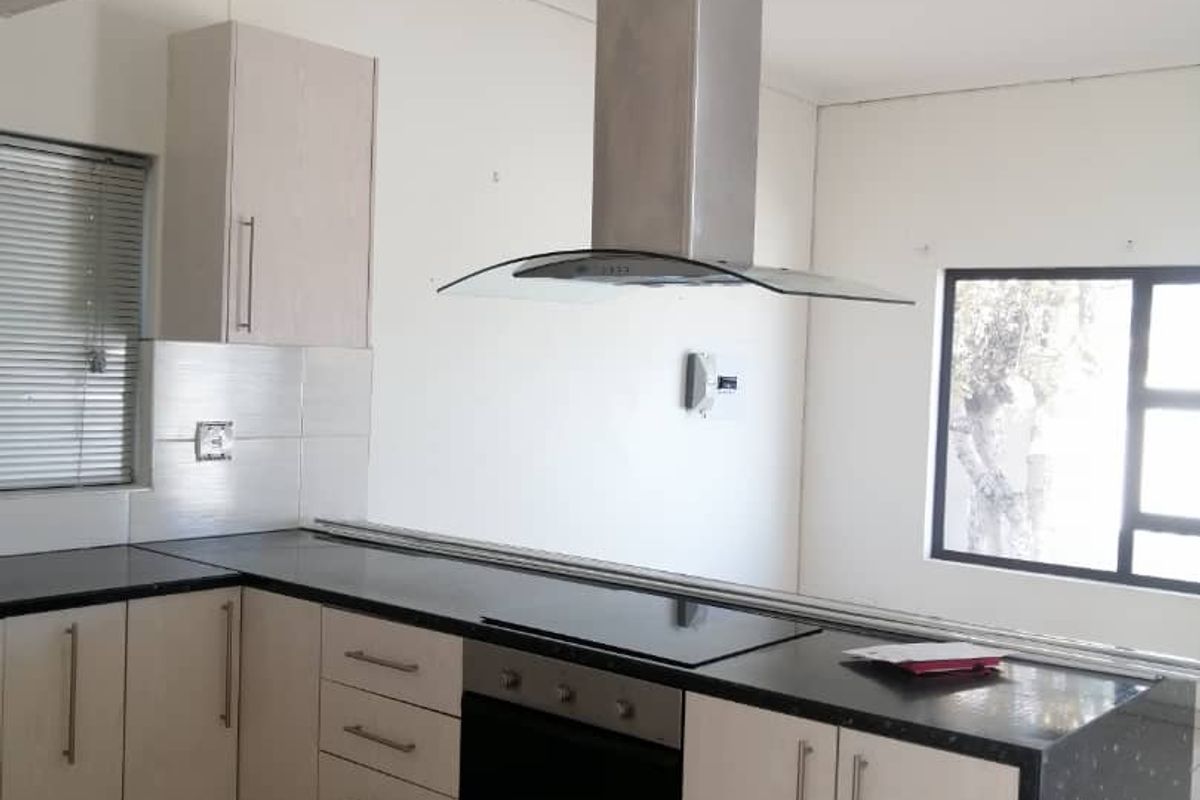 A functional kitchen featuring light-toned cabinetry, dark countertops, a built-in oven, and a stainless steel extractor fan.