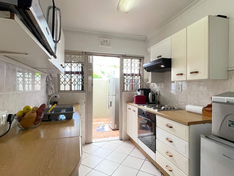 Functional kitchen featuring built-in cabinetry, laminate countertops, integrated oven and hob, tiled backsplash, and direct access to an outdoor area.