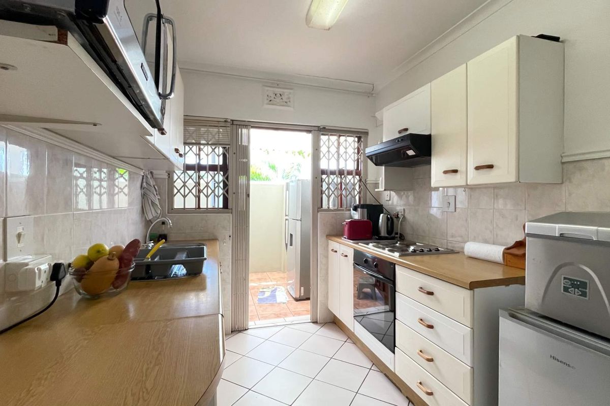 Functional kitchen featuring built-in cabinetry, laminate countertops, integrated oven and hob, tiled backsplash, and direct access to an outdoor area.