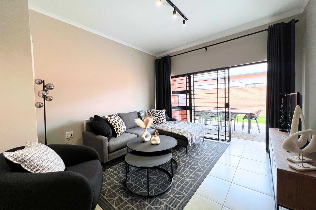 A well-maintained living room featuring tiled flooring, track lighting, and large sliding glass doors that provide direct access to an outdoor patio area.