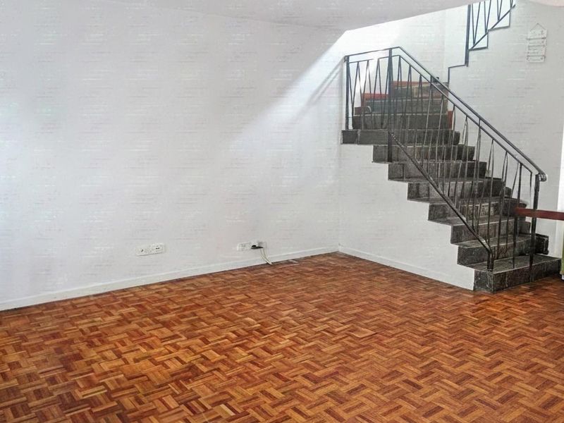 An empty living area featuring classic parquet flooring and a staircase with a metal balustrade, offering a blank canvas for interior design.