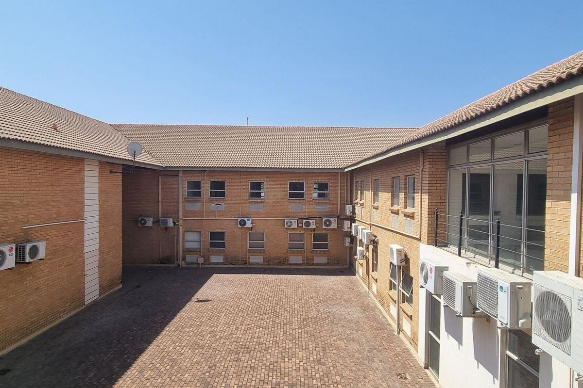 An exterior view of an office building courtyard featuring brick facade, tiled roofing, and multiple wall-mounted air conditioning units.