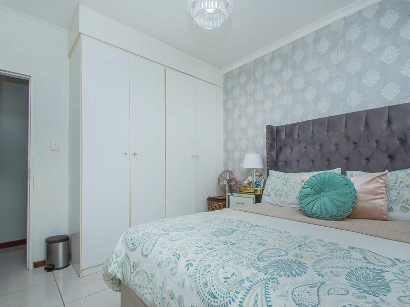 A well-maintained bedroom featuring built-in cupboards, tiled flooring, and a decorative wallpaper feature wall.