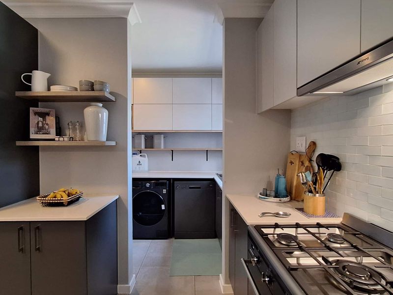 Modern kitchen featuring stone countertops, subway tile backsplash, gas hob with extractor, and a separate scullery area with built-in cabinetry.