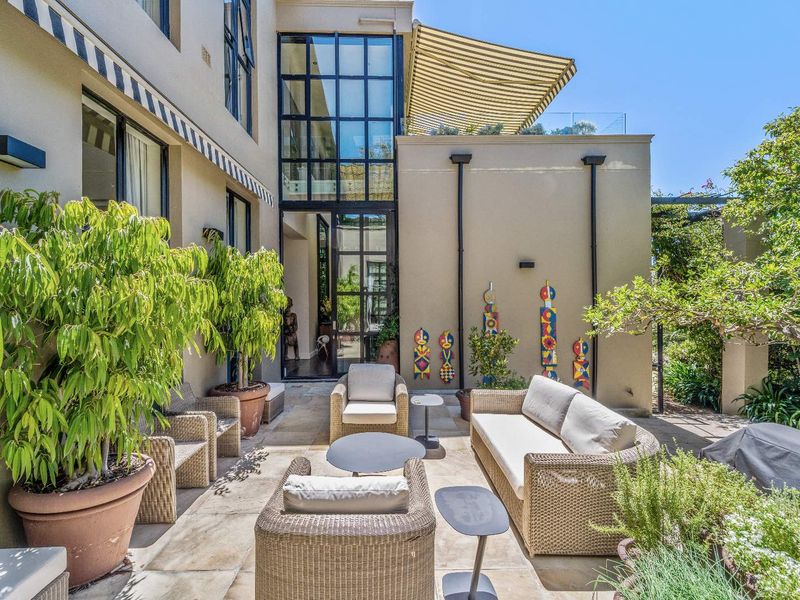 A spacious outdoor patio area featuring stone paving, retractable awnings, and large floor-to-ceiling glass windows providing access to the interior.