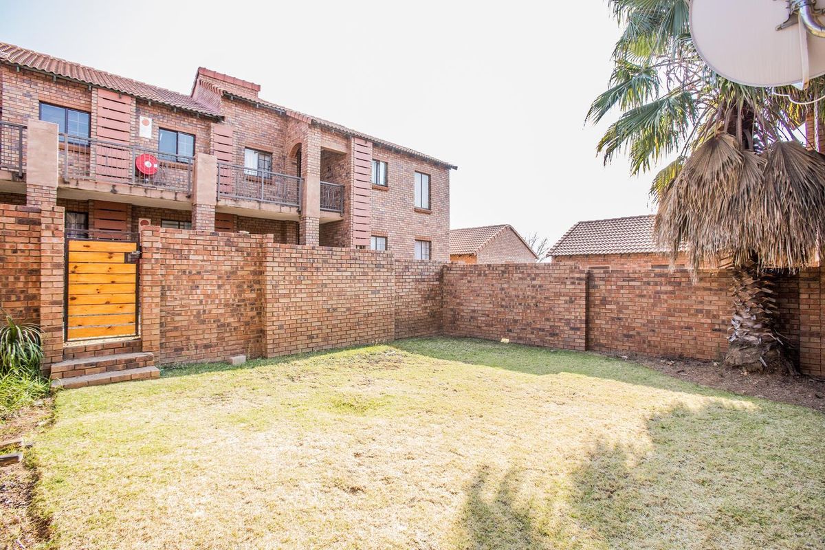 A private rear garden area featuring a brick boundary wall, lawn space, and access to the townhouse building with balconies.